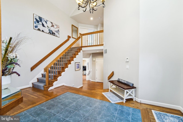 stairway with wood-type flooring, a towering ceiling, and a notable chandelier