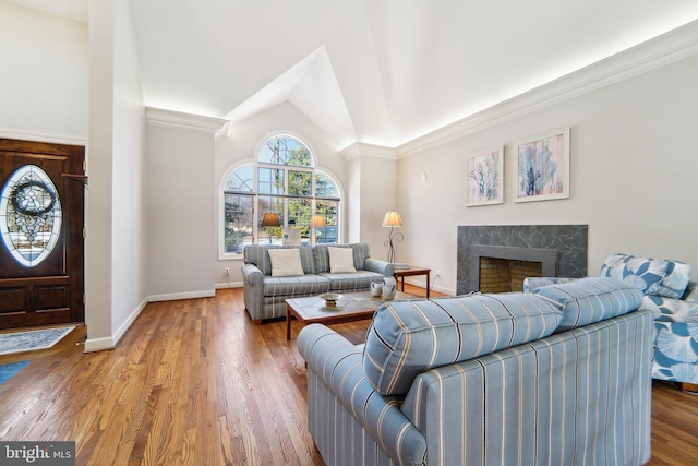 living room with hardwood / wood-style flooring, vaulted ceiling, ornamental molding, and a fireplace