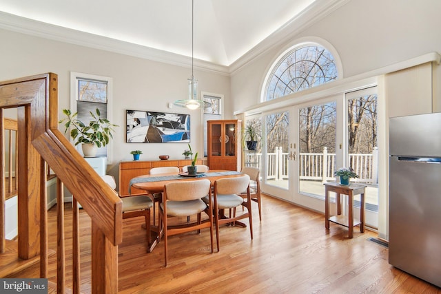 dining space with light hardwood / wood-style flooring, ornamental molding, french doors, and a high ceiling