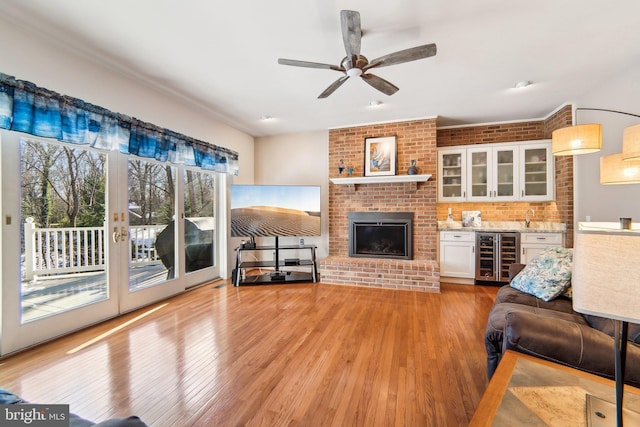 living room featuring wine cooler, ceiling fan, a brick fireplace, light wood-type flooring, and french doors