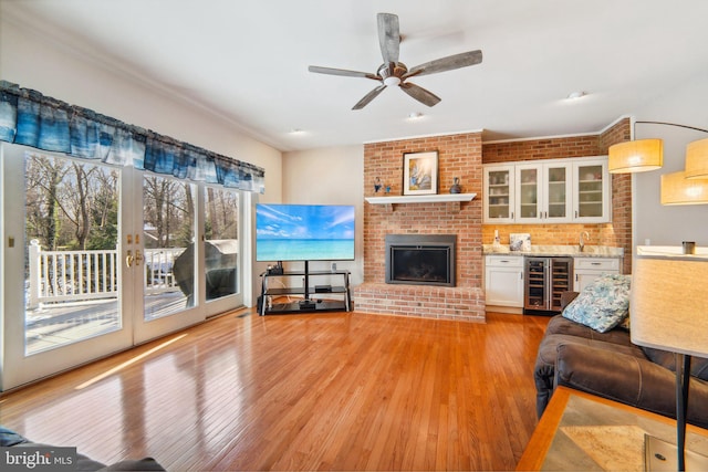 living room featuring wine cooler, light hardwood / wood-style flooring, ceiling fan, brick wall, and a fireplace