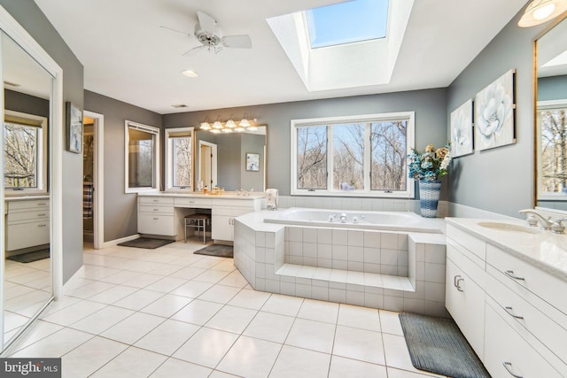 bathroom with a relaxing tiled tub, vanity, a skylight, and tile patterned flooring