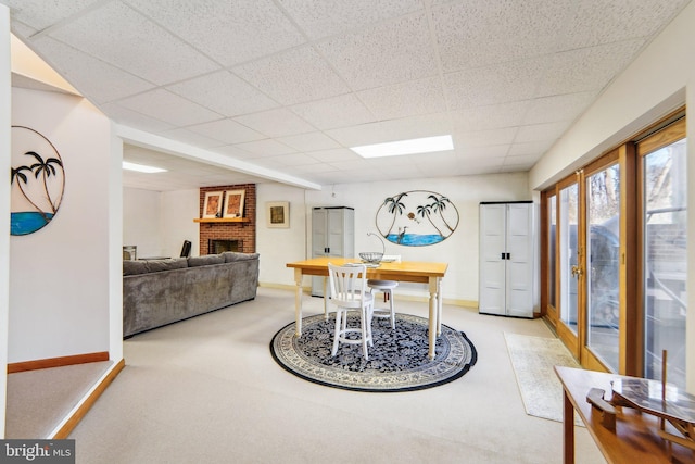 dining space featuring a brick fireplace, light carpet, and a drop ceiling