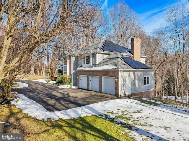 view of snow covered exterior with a garage and solar panels