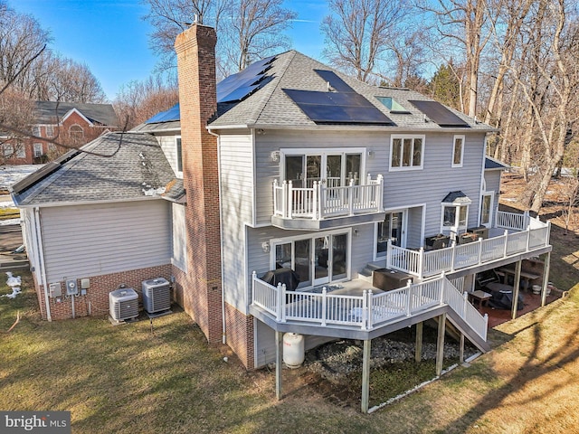 rear view of property featuring solar panels, a balcony, central AC unit, a lawn, and a wooden deck