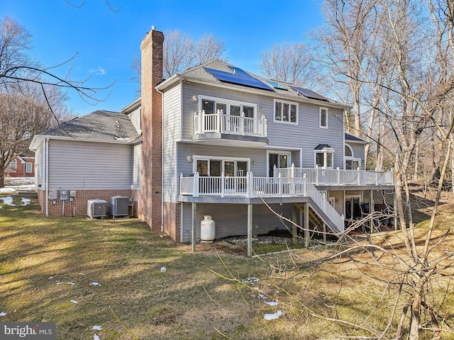 back of house with central AC unit, a lawn, solar panels, and a deck