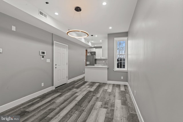 kitchen with wood-type flooring, stainless steel fridge, hanging light fixtures, backsplash, and white cabinetry