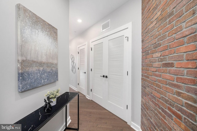 hallway with brick wall and dark wood-type flooring