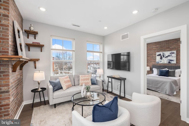 living room with a brick fireplace, dark wood-type flooring, and brick wall