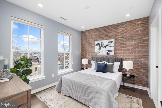 bedroom with dark wood-type flooring and brick wall