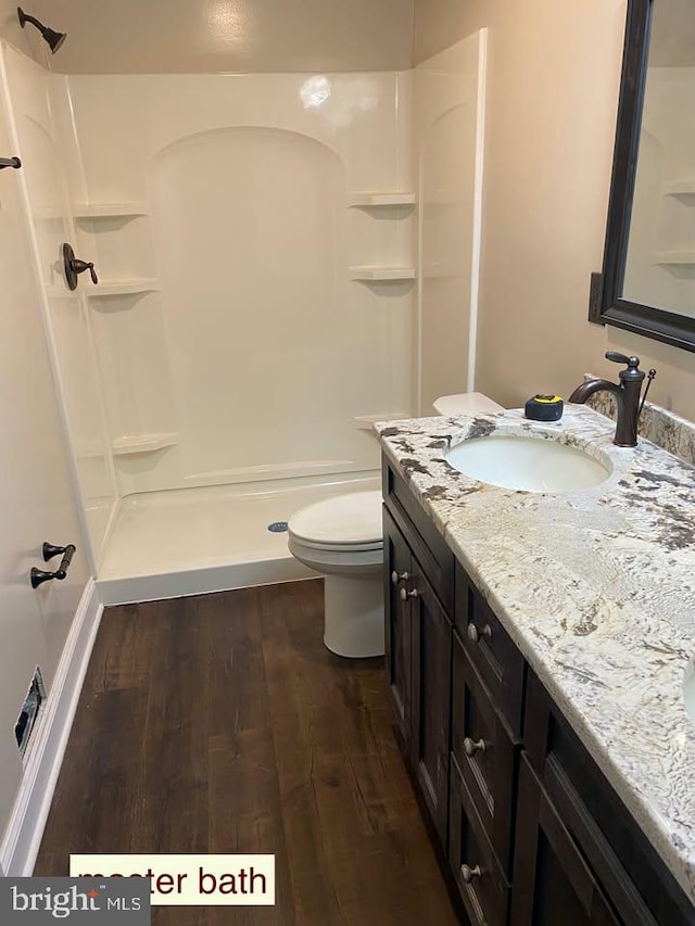 bathroom with hardwood / wood-style flooring, vanity, toilet, and a shower