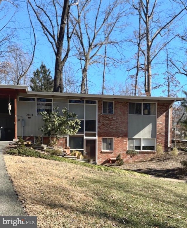 view of front of property with a front yard, brick siding, driveway, and a sunroom