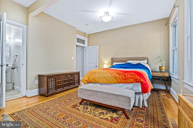 bedroom featuring beamed ceiling, hardwood / wood-style flooring, connected bathroom, and multiple windows