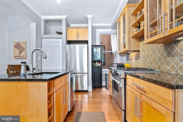 kitchen with crown molding, appliances with stainless steel finishes, sink, dark stone countertops, and a center island with sink