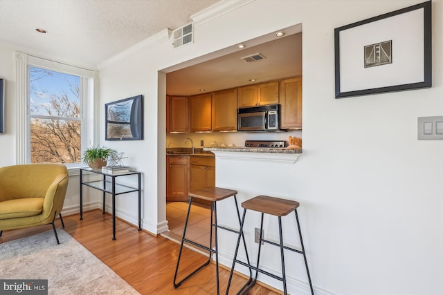 kitchen with a breakfast bar, light wood-type flooring, ornamental molding, light stone countertops, and a textured ceiling