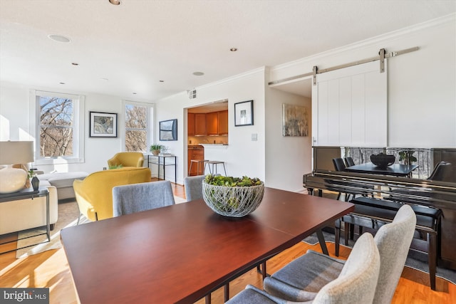 dining space with crown molding, a barn door, and light hardwood / wood-style flooring