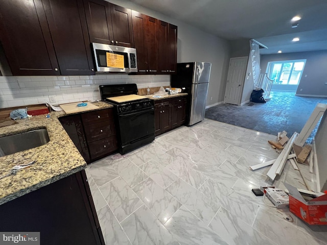 kitchen with appliances with stainless steel finishes, sink, backsplash, light stone counters, and dark brown cabinets