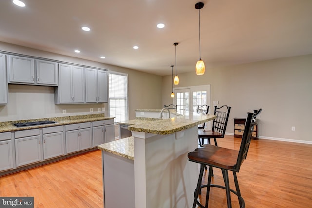 kitchen with hanging light fixtures, a kitchen island with sink, a kitchen bar, and light hardwood / wood-style flooring