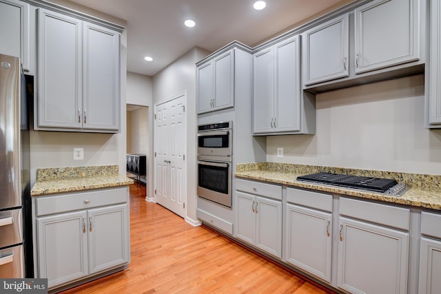 kitchen with light stone counters, gray cabinetry, light hardwood / wood-style floors, and appliances with stainless steel finishes