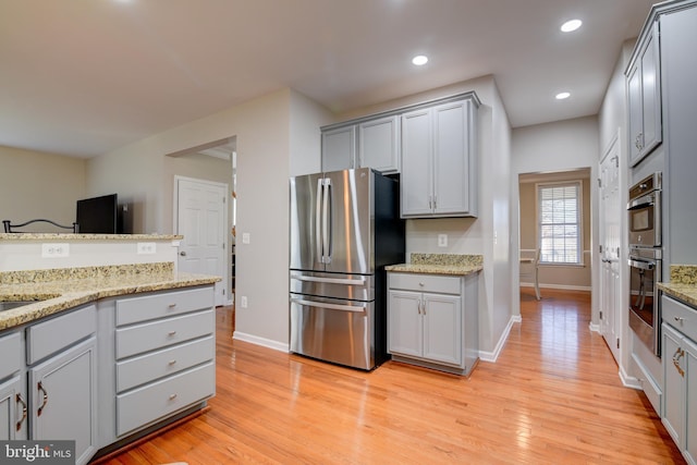 kitchen with sink, gray cabinetry, light wood-type flooring, stainless steel appliances, and light stone countertops