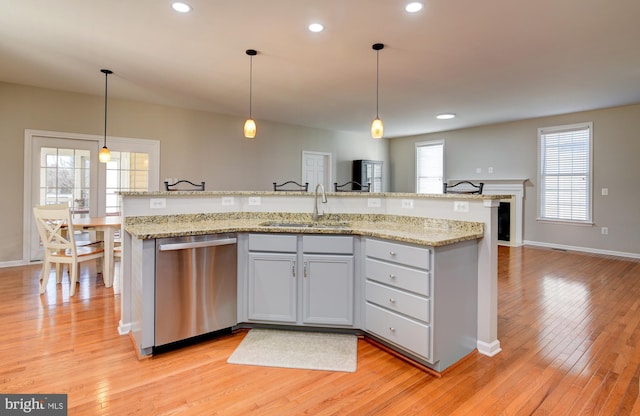 kitchen with sink, decorative light fixtures, light wood-type flooring, stainless steel dishwasher, and an island with sink