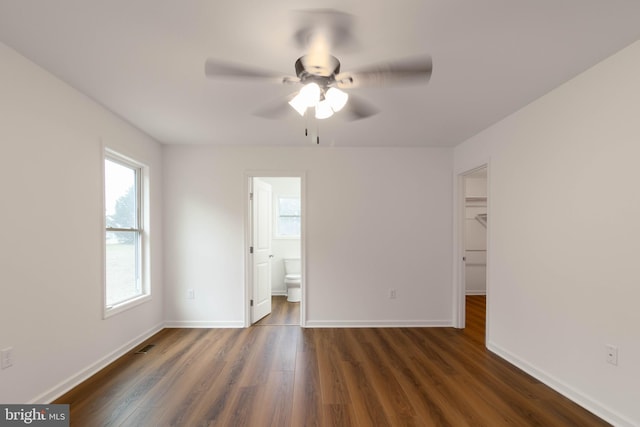 unfurnished bedroom featuring a spacious closet, ensuite bath, a closet, ceiling fan, and dark hardwood / wood-style floors