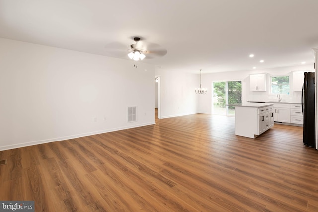 unfurnished living room with ceiling fan with notable chandelier, sink, and hardwood / wood-style floors