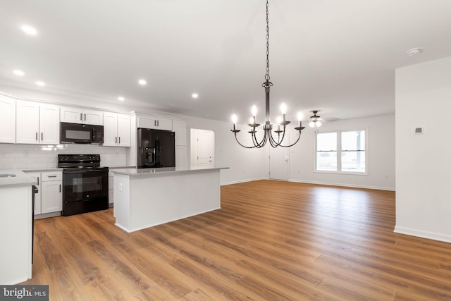 kitchen featuring decorative light fixtures, backsplash, white cabinets, a kitchen island, and black appliances