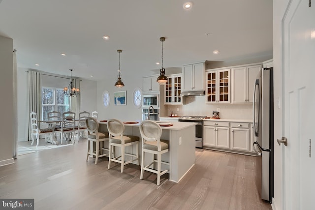 kitchen with appliances with stainless steel finishes, a kitchen island with sink, pendant lighting, light hardwood / wood-style floors, and white cabinets