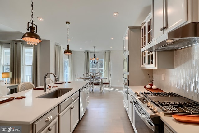 kitchen featuring sink, stainless steel appliances, an island with sink, decorative light fixtures, and light wood-type flooring