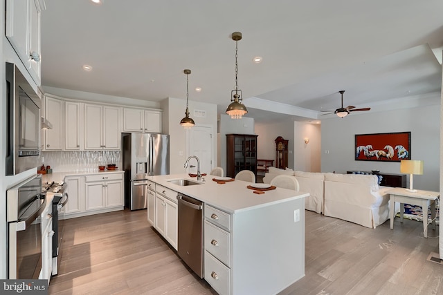 kitchen with white cabinetry, decorative light fixtures, a center island with sink, stainless steel appliances, and decorative backsplash