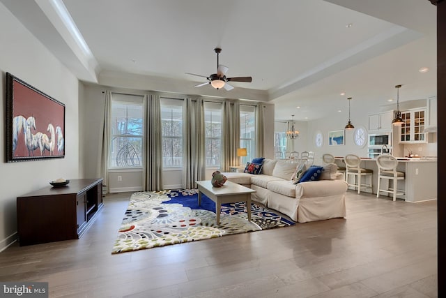 living room featuring a raised ceiling, wood-type flooring, ornamental molding, and ceiling fan with notable chandelier