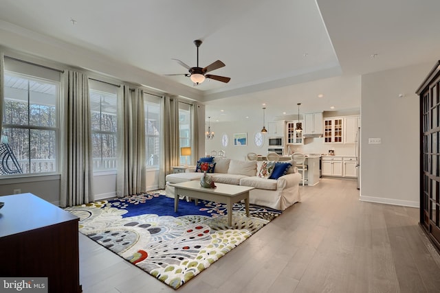 living room featuring a tray ceiling, ceiling fan with notable chandelier, and light hardwood / wood-style flooring