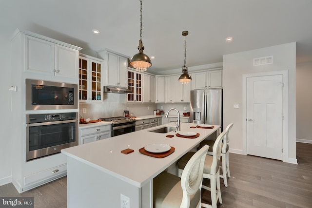 kitchen featuring stainless steel appliances, an island with sink, hanging light fixtures, and sink