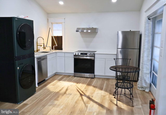 kitchen featuring sink, white cabinetry, light wood-type flooring, stainless steel appliances, and stacked washing maching and dryer