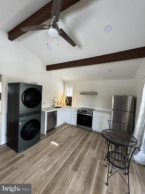 kitchen featuring vaulted ceiling with beams, appliances with stainless steel finishes, stacked washing maching and dryer, light hardwood / wood-style floors, and white cabinets