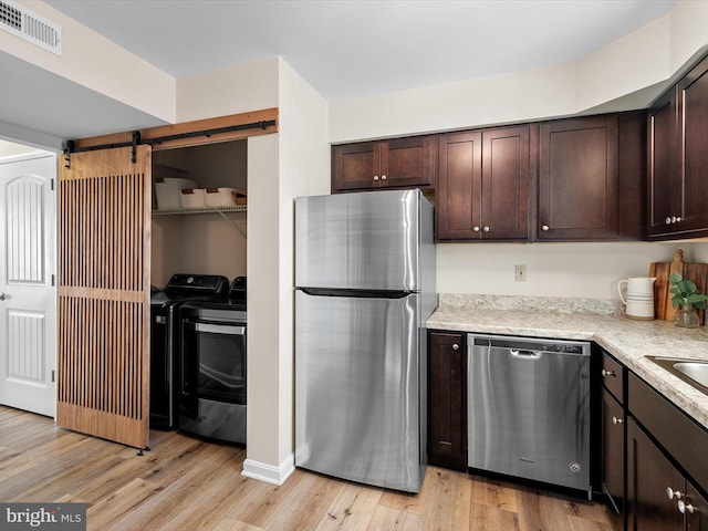 kitchen with a barn door, appliances with stainless steel finishes, dark brown cabinets, and light wood-type flooring