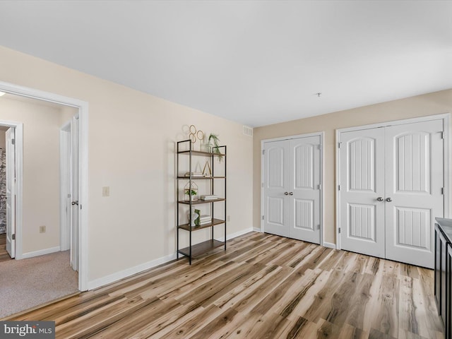 unfurnished bedroom with two closets and light hardwood / wood-style flooring