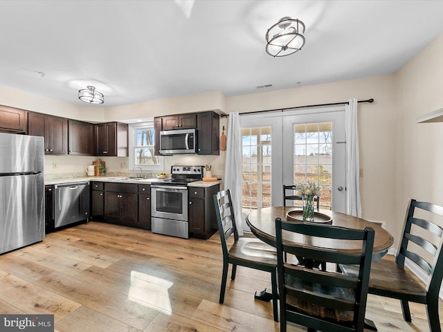 kitchen with stainless steel appliances, dark brown cabinets, sink, and light hardwood / wood-style flooring