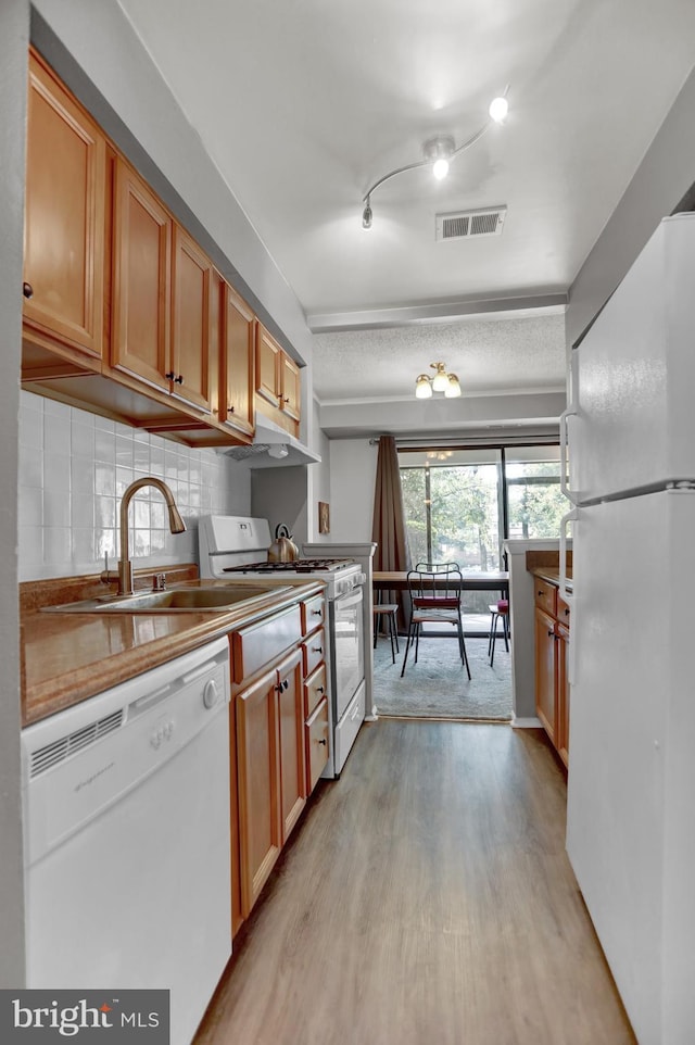 kitchen featuring sink, white appliances, light hardwood / wood-style flooring, and decorative backsplash