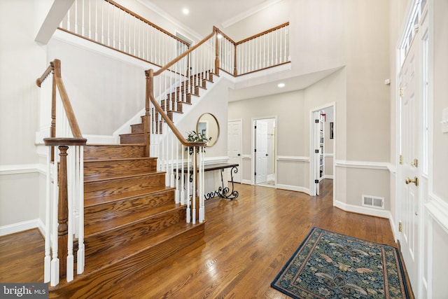 foyer with crown molding, a towering ceiling, and hardwood / wood-style flooring