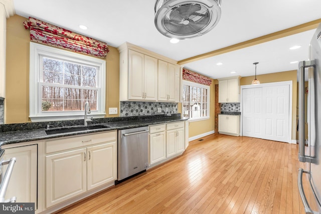 kitchen with sink, hanging light fixtures, dark stone countertops, appliances with stainless steel finishes, and light hardwood / wood-style floors