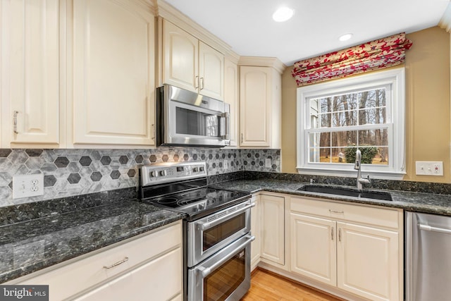 kitchen featuring appliances with stainless steel finishes, sink, dark stone countertops, backsplash, and light hardwood / wood-style flooring