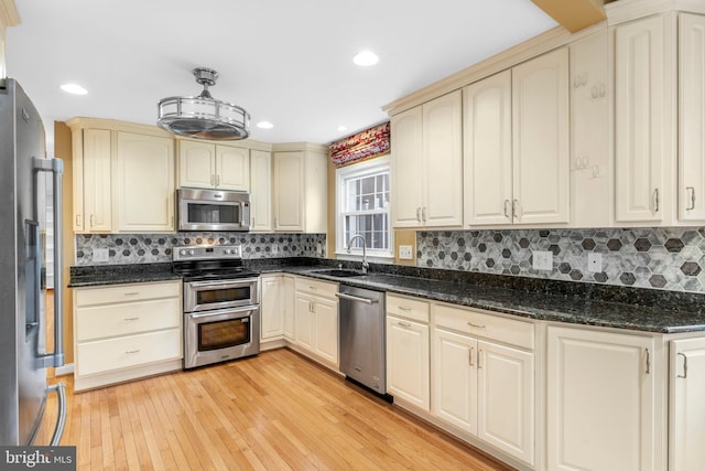 kitchen featuring sink, light hardwood / wood-style flooring, stainless steel appliances, cream cabinets, and dark stone counters