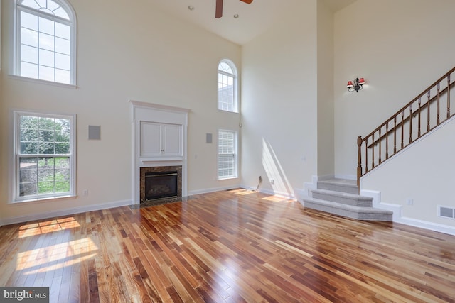 unfurnished living room featuring a towering ceiling, light hardwood / wood-style flooring, a high end fireplace, and ceiling fan