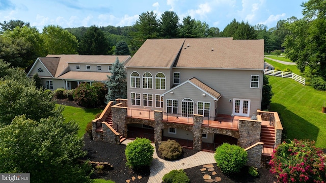 rear view of property with french doors, a wooden deck, a garage, and a lawn