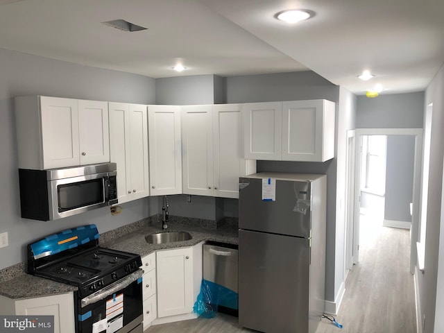 kitchen featuring sink, light hardwood / wood-style flooring, dark stone countertops, stainless steel appliances, and white cabinets