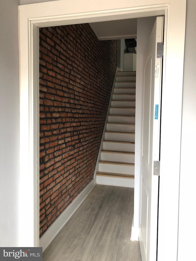 stairs featuring hardwood / wood-style flooring and brick wall