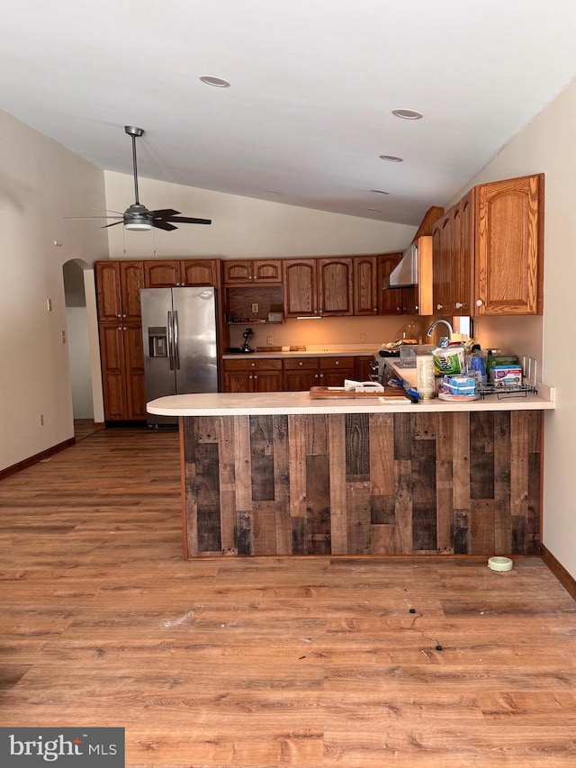 kitchen featuring light hardwood / wood-style floors, wall chimney exhaust hood, kitchen peninsula, and stainless steel fridge with ice dispenser