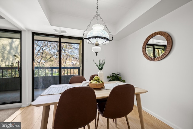 dining space with light wood-type flooring and a tray ceiling